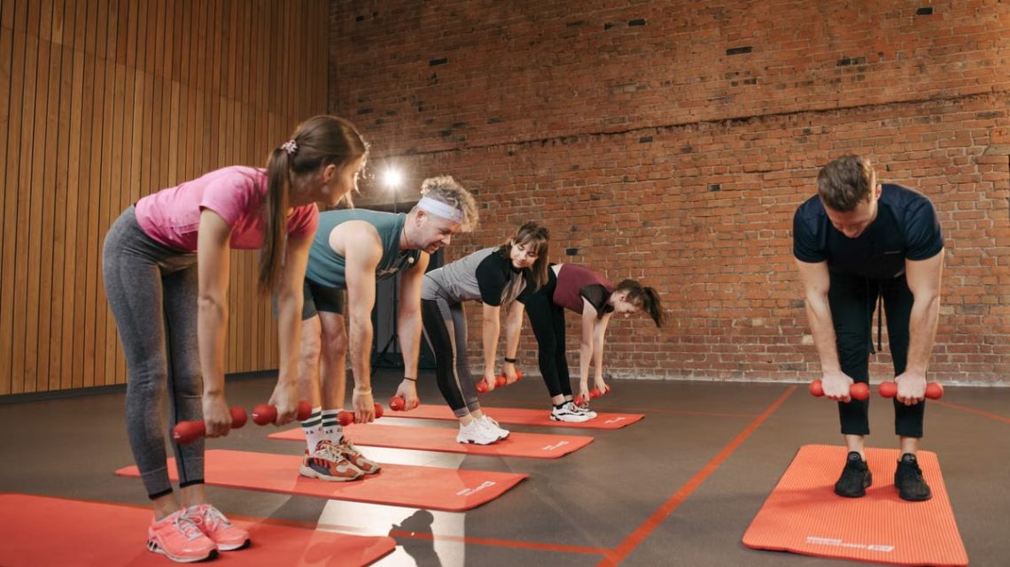 Fitness group performing exercises with dumbbells in a modern yoga studio setting.