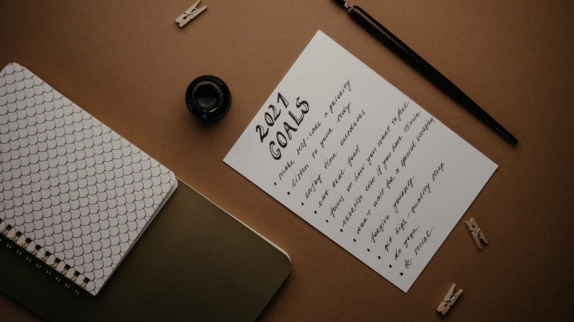 Stylish flat lay of a 2021 goals list with stationery on a brown background.