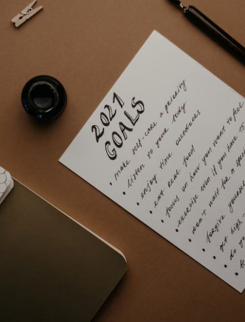 Stylish flat lay of a 2021 goals list with stationery on a brown background.